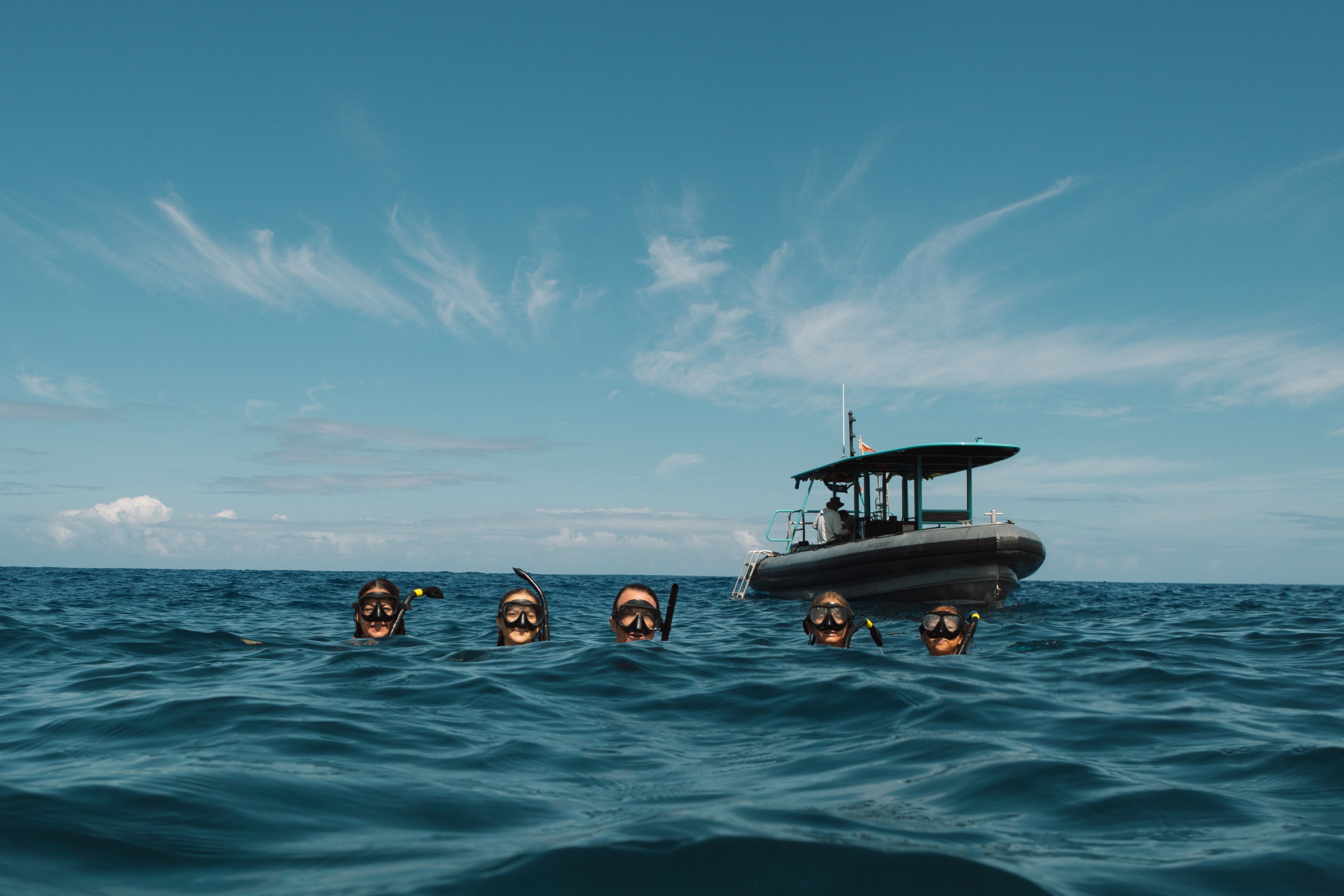 Four snorkelers in ocean near a boat under a clear blue sky.