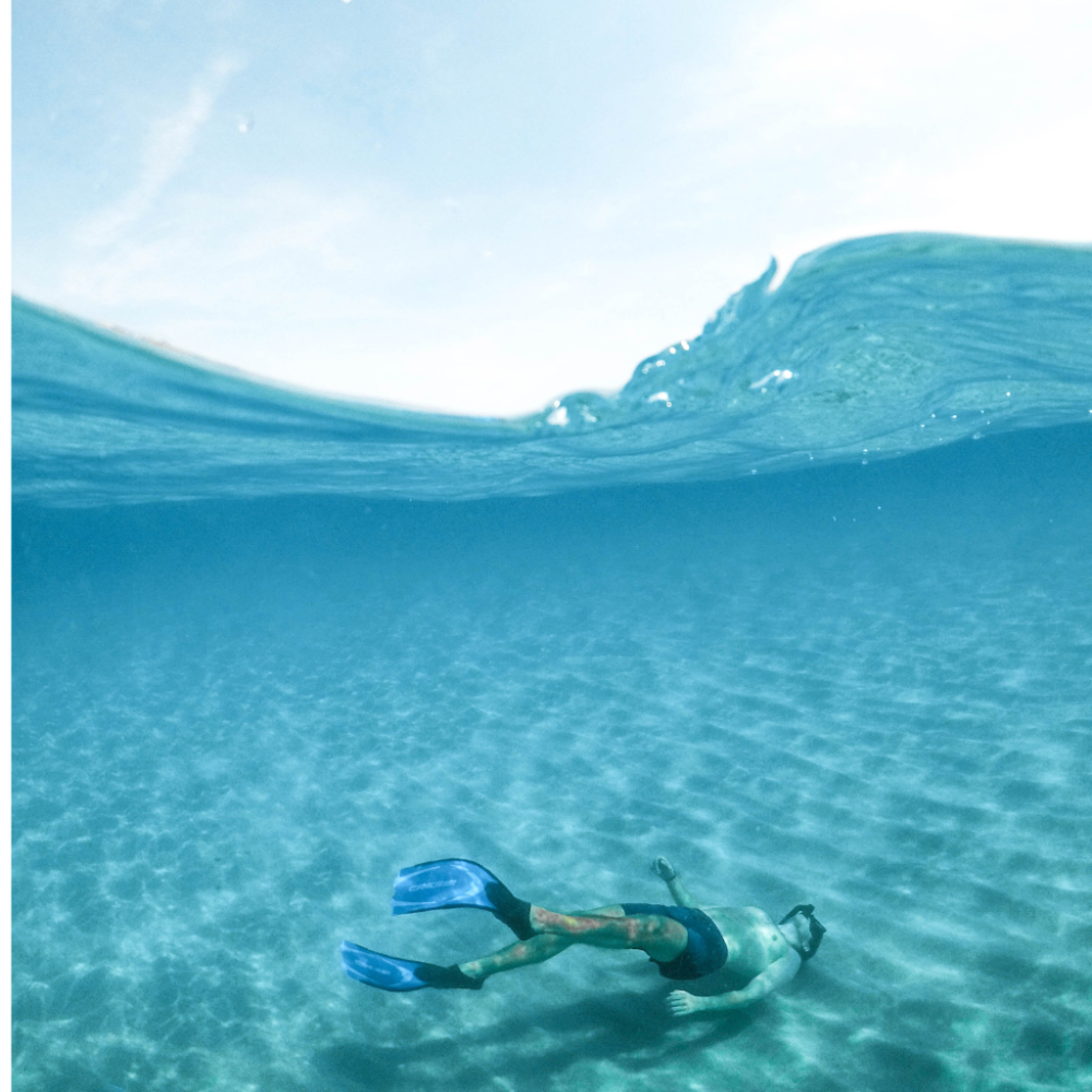 Underwater view of a snorkeler swimming with fins in clear blue water.