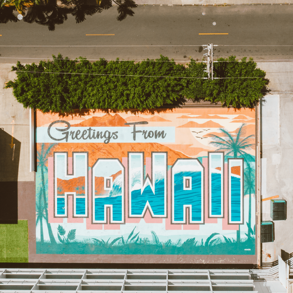 Aerial view of a colorful 'Greetings from Hawaii' mural with tropical designs.