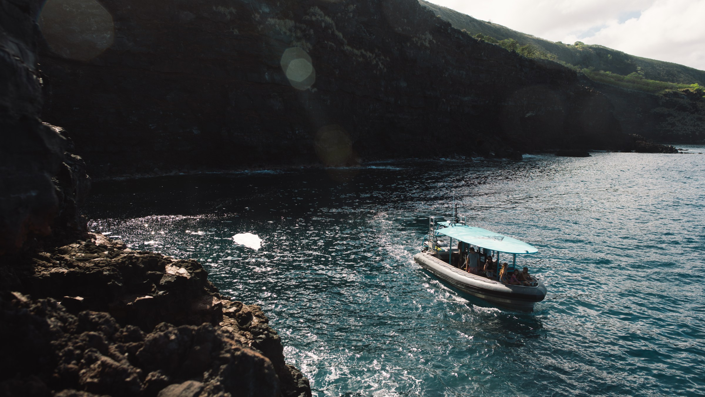 Boat with blue canopy on ocean near rocky coastline.