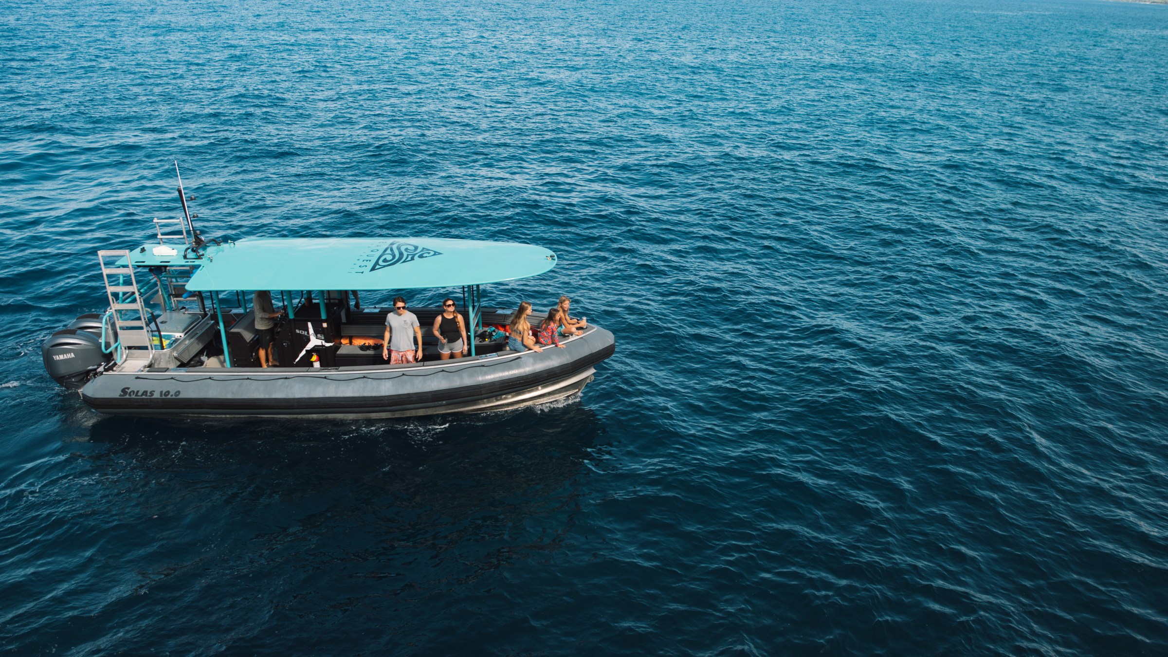 A small boat with people on it floats on the blue ocean, under a clear sky.