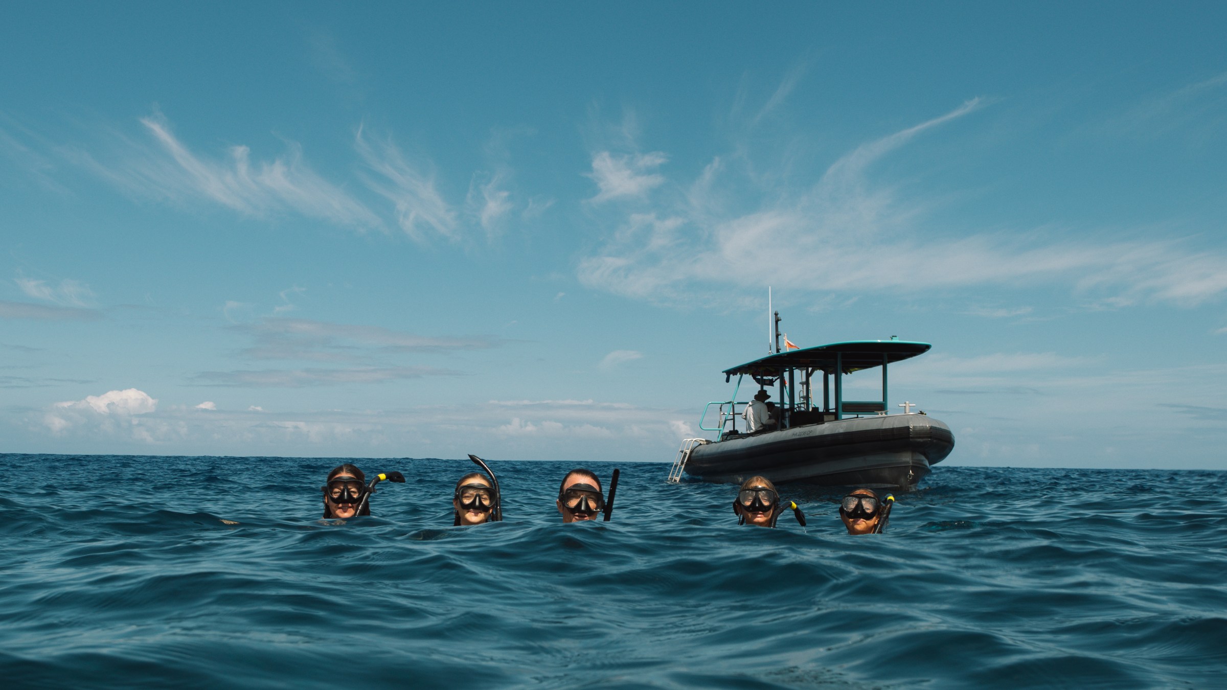 Four snorkelers in the ocean near a black boat under a clear blue sky.