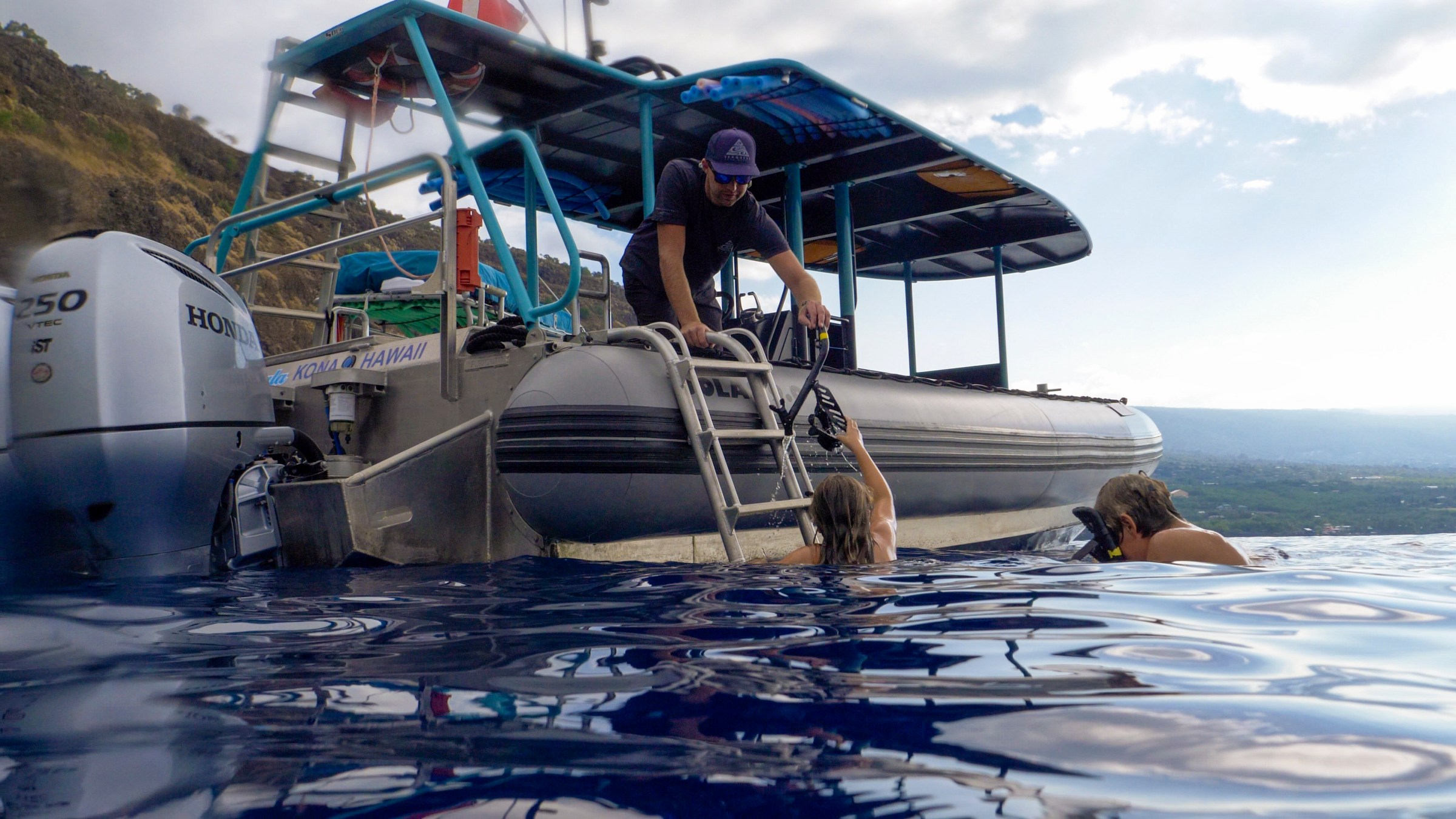 People climbing aboard a boat from the water, with a mountainous coastline in the background.