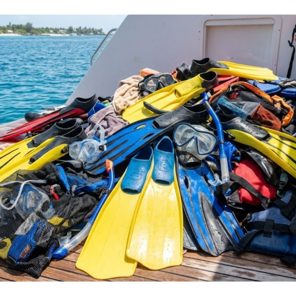 Piles of snorkeling gear with yellow and blue fins on a boat deck by the sea.