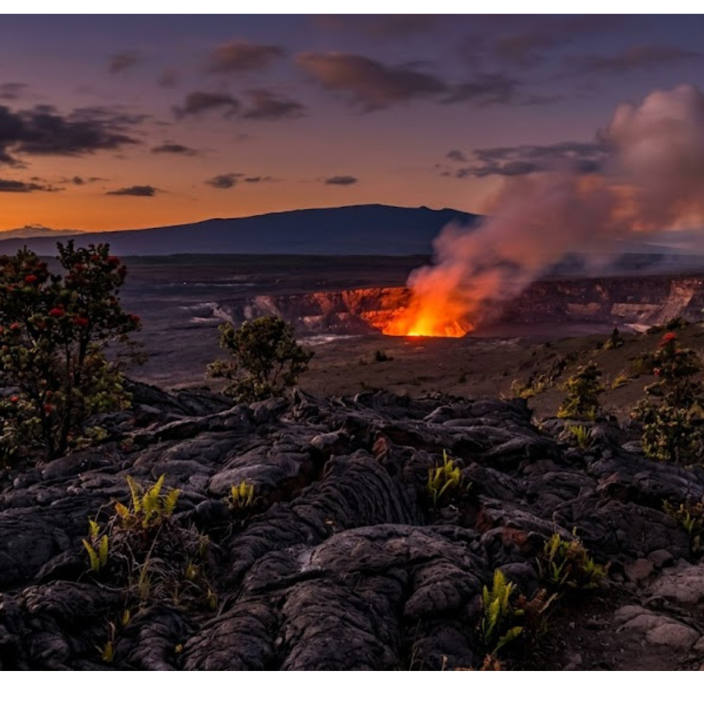 Glowing volcanic crater with smoke, surrounded by rocks and vegetation at dusk.