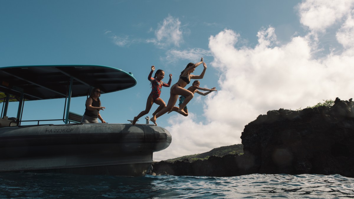 Four people jumping off a boat into the water, under a partly cloudy sky.