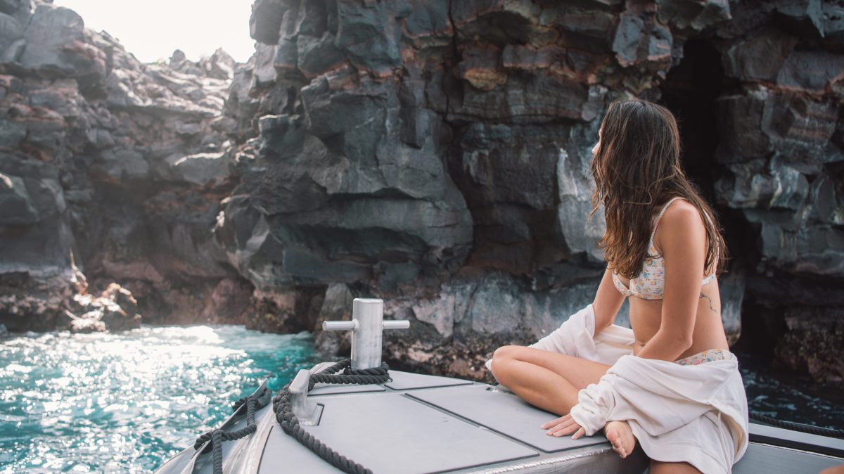 Woman on a boat near rocky cliffs, looking towards the sea.
