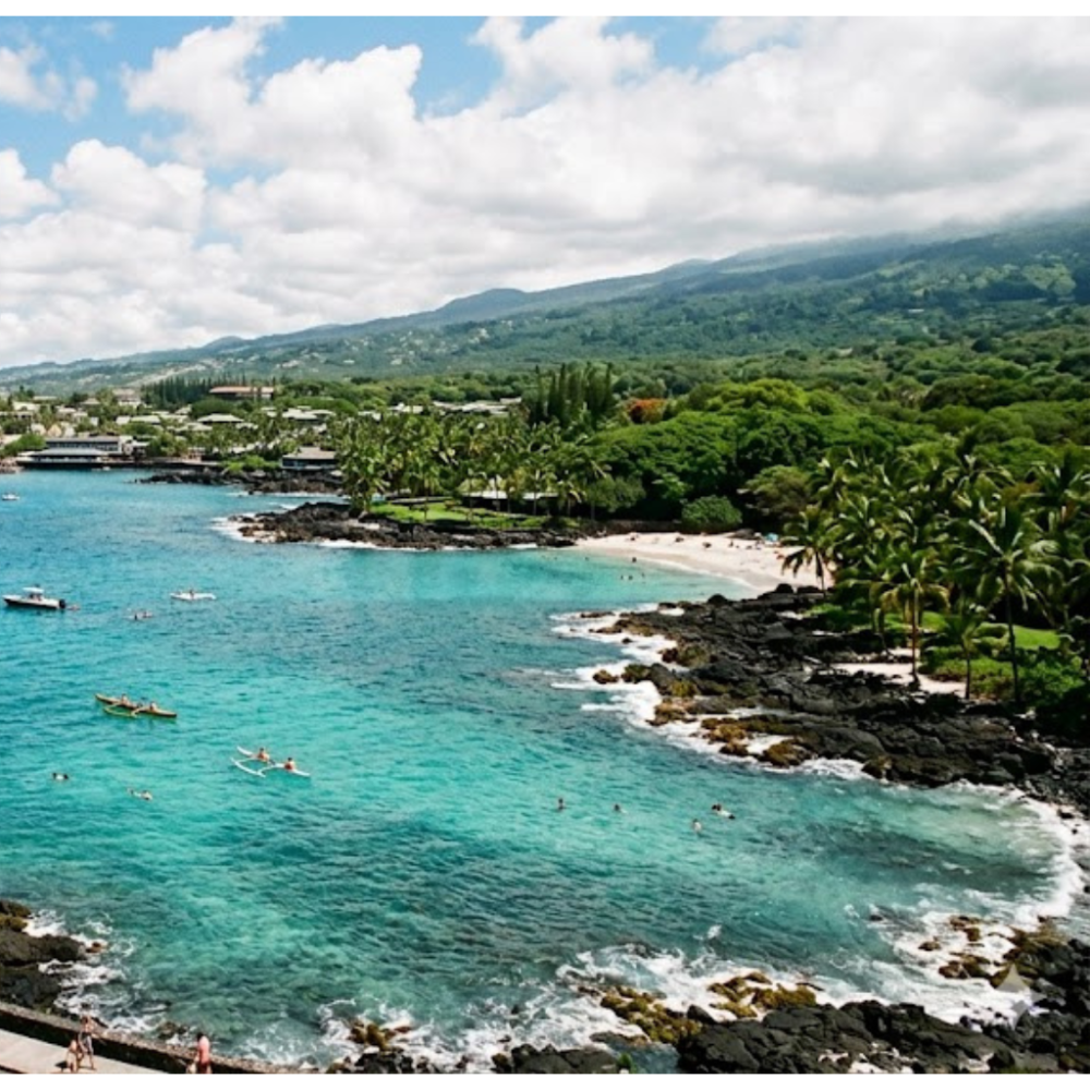 A scenic beach with turquoise waters, scattered clouds, and lush greenery in the background.
