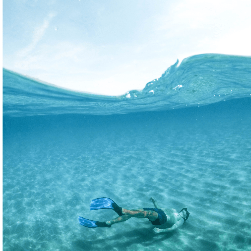 Person snorkeling underwater over sandy ocean floor.